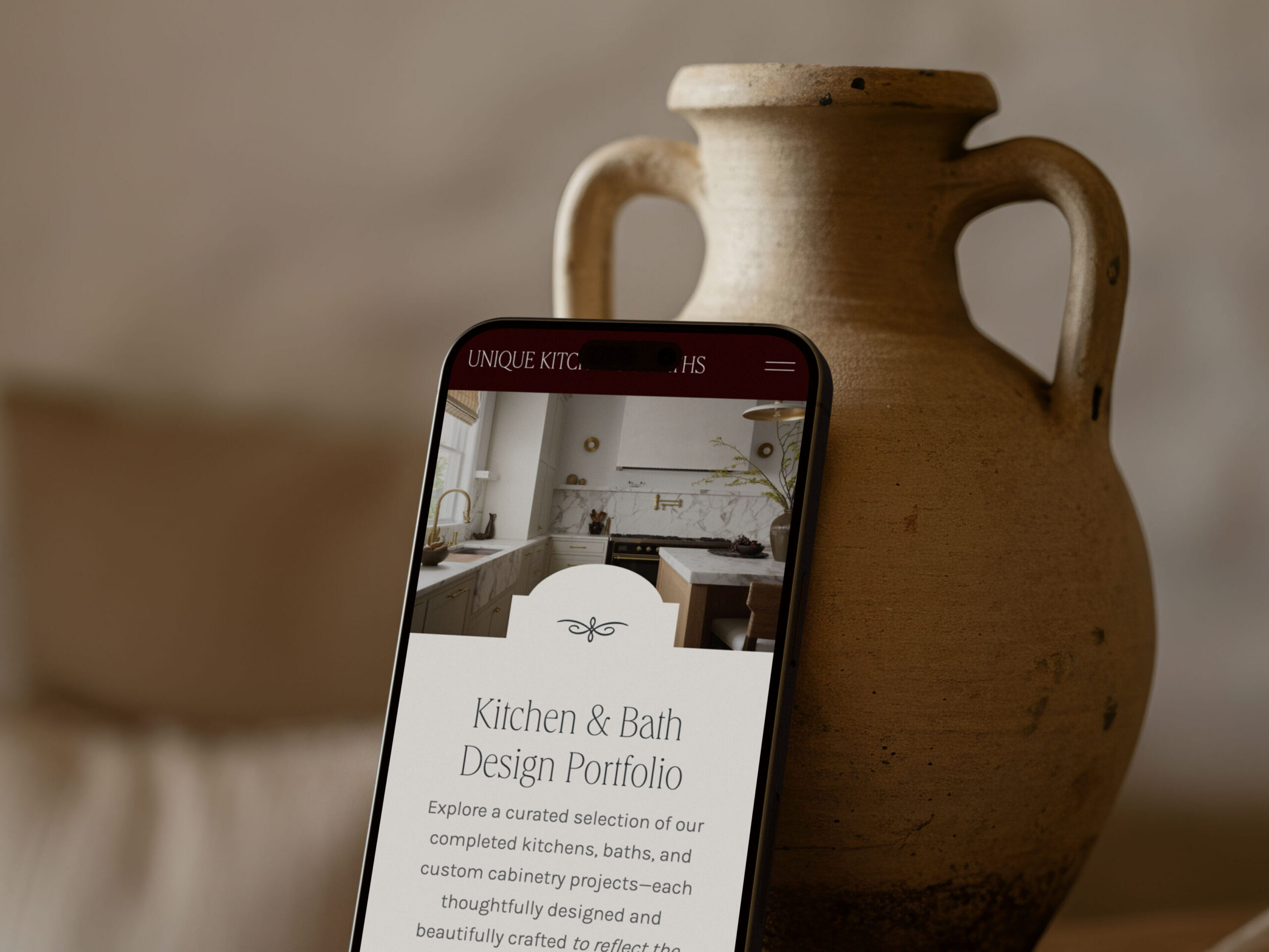 Smartphone displaying a luxury interior designer website beside a ceramic vase, showcasing an elevated mobile browsing experience.